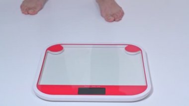 Orta yaşlı obez bir kadın çıplak ayakla tartıldığı için tartıda duruyor. Yan görünüm.