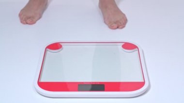 Orta yaşlı obez bir kadın çıplak ayakla tartıldığı için tartıda duruyor. Yan görünüm.