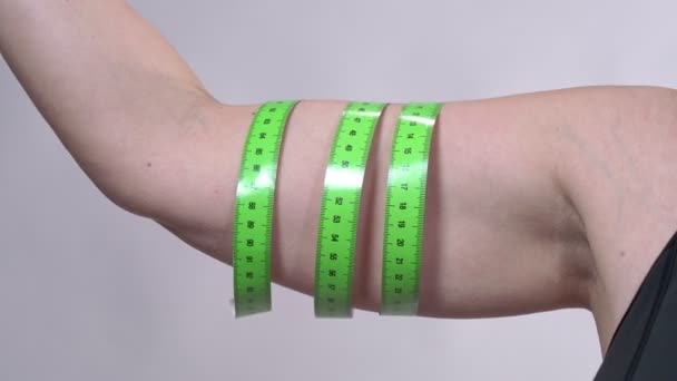 Una mujer de mediana edad con la piel flácida determina la circunferencia de su mano con una cinta métrica, sobre un fondo blanco . — Vídeos de Stock