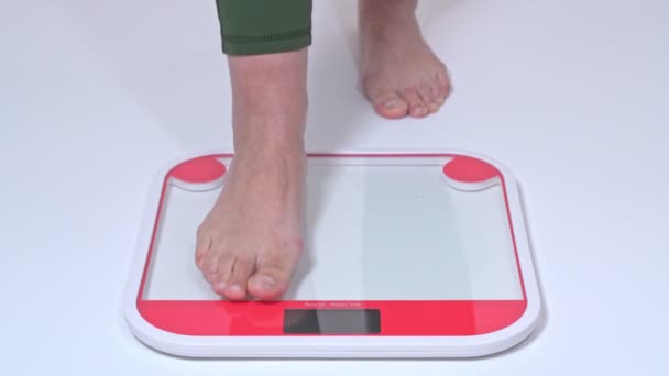 Женщина среднего возраста с ожирением стоит на весах за то, что взвешивает босыми ногами. Вид сбоку . — стоковое видео