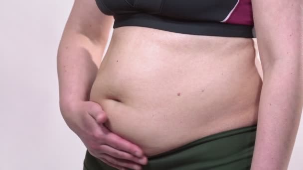 Une femme d'âge moyen avec une peau affaissée caressant un gros ventre, sur un fond blanc. Plan latéral . — Video