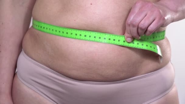 A middle-aged woman with saggy skin defines her large belly with a measuring tape with turns, on a white background. Side plan. — Stock Video