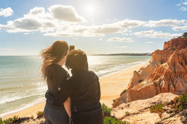 Dwie sportowe dziewczyny, na skalistym brzegu, zrobić zdjęcie selfie, odnoszący sukcesy biznesmeni sortuje Ocean Atlantycki Portugalia, Falesia Algarve. — Zdjęcie stockowe