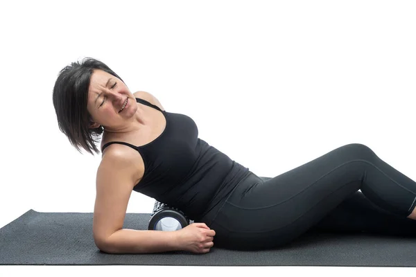 Una donna di mezza età, su un tappeto da ginnastica con rullo miofasciale, sta sperimentando mal di schiena, su uno sfondo bianco . — Foto Stock