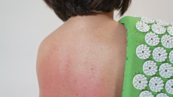 A middle-aged woman punches her red back from a massage for pain in the back and spine on an acupuncture rug. Close-up. — Stock Video