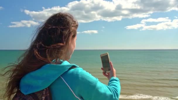 Молода дівчина турист на пляжі біля океану з телефоном в руці зробить фотографії ландшафту навколо нього . — стокове відео