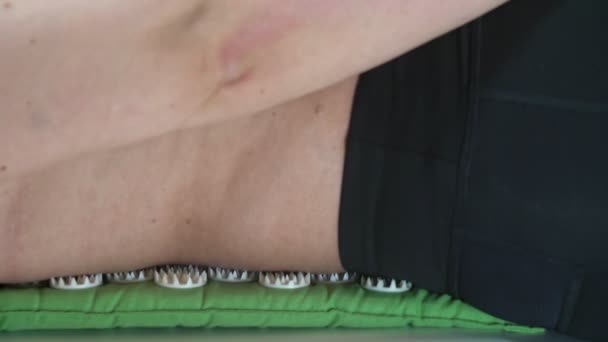 Una donna di mezza età si alza da un tappeto di agopuntura con la schiena nuda su cui stava facendo un massaggio. Primo piano . — Video Stock