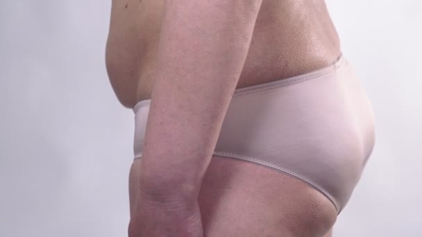 Una donna di mezza età con la pelle cadente si gira ai lati e mostra la sua grande pancia, su uno sfondo bianco. Piano laterale . — Video Stock