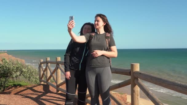 Succesvolle vrouw van middelbare leeftijd met een jong meisje, op een klif in de buurt van de oceaan, selfie per telefoon. Portugal. Het is Vilamoura. Moeder met dochter. — Stockvideo