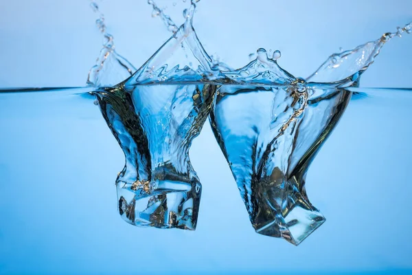 Abstraktní, minimalistický cákanec vody s kostkami ledu. Bubliny na modrém pozadí. — Stock fotografie