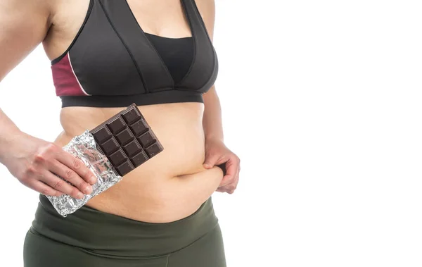 手にチョコレートで彼女の胃に余分な脂肪を持つ女性.肥満の概念的なイメージ。サイドビュー。白い背景に隔離された. — ストック写真