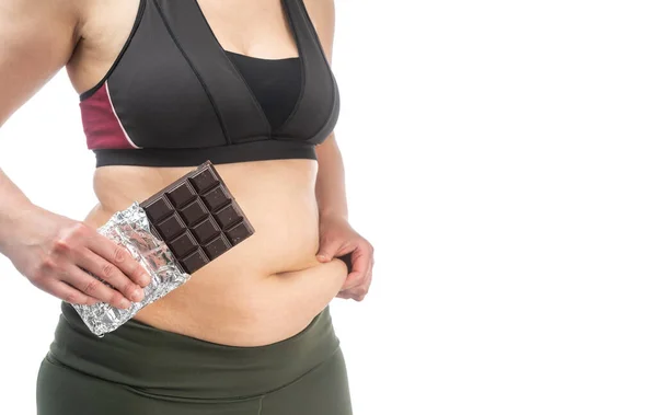 Vrouw met overtollig vet op haar buik met chocolade in de hand. Conceptueel beeld van obesitas. Zijaanzicht. Geïsoleerd op een witte achtergrond. — Stockfoto