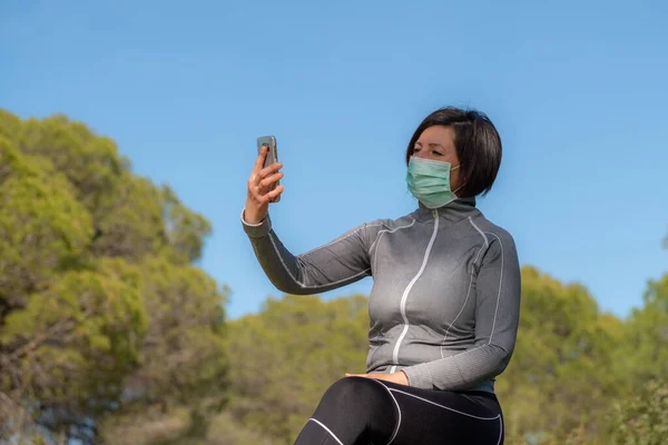 Menina no período de coronavírus em uma máscara atrás de um telefone na natureza. Isolamento social . — Fotografia de Stock