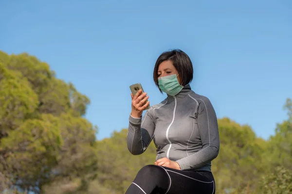 Menina no período de coronavírus em uma máscara atrás de um telefone na natureza. Isolamento social . — Fotografia de Stock