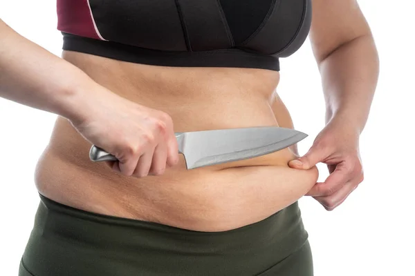 Žena středního věku s obezitou a povislou kůží břicha, na bílém pozadí, zblízka. Nůž, symbol plastické chirurgie. — Stock fotografie