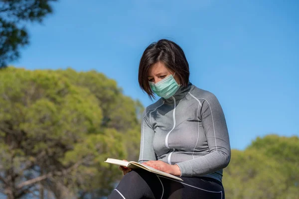 Κορίτσι στην περίοδο ενός κορωναϊού με μάσκα που διάβαζε ένα βιβλίο στη φύση. Κοινωνική απομόνωση. Μείνε σπίτι.. — Φωτογραφία Αρχείου