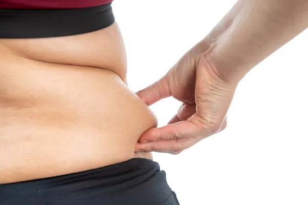 A middle-aged woman holds a fold of fat on her waist. Conceptual image of obesity. Back view. Close-up, Isolated on a white background. — Stock Photo, Image
