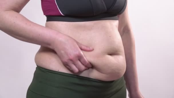 Žena středního věku s povislou kůží na břiše ukazuje čokoládu. Na bílém pozadí. — Stock video