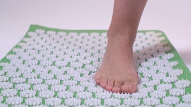 Wanita berdiri dengan satu kaki di atas tikar pijat akupuntur. Close-up. — Stok Video