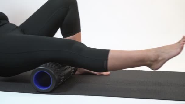 En medelålders kvinna på en myofascial roller gör en ben skenmassage på en vit bakgrund. — Stockvideo