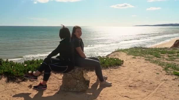 Lyckad, glad medelålders kvinna med en ung flicka, på en klippa nära havet, trött, satte sig ner för att vila på en sten. Portugal. Det är Vilamoura. Mor med dotter. — Stockvideo