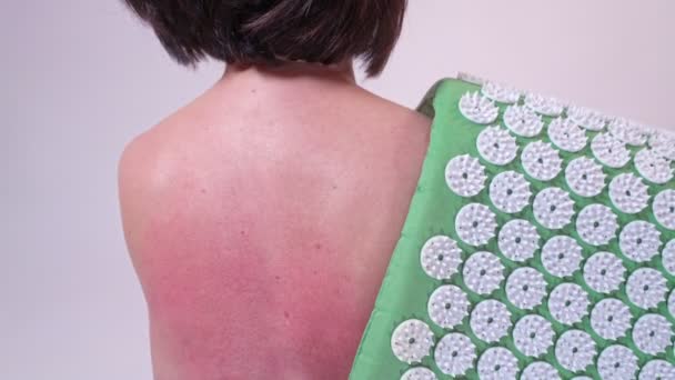 A middle-aged woman punches her red back from a massage for pain in the back and spine on an acupuncture rug. Close-up. — Stock Video