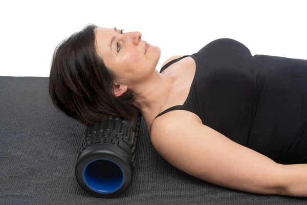 Eine Frau mittleren Alters mit schlaffer Haut auf einer Gymnastikmatte mit Myofaszienrolle macht auf ihrem Rücken vor weißem Hintergrund eine Übung. — Stockfoto