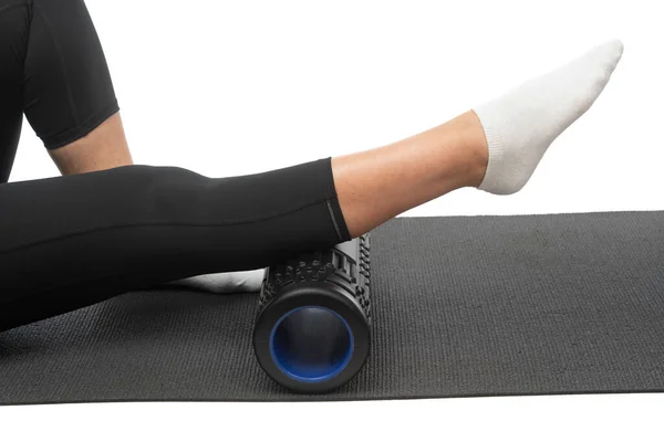 Een vrouw van middelbare leeftijd op een myofasciale roller doet een been scheenbeen massage op een witte achtergrond. — Stockfoto