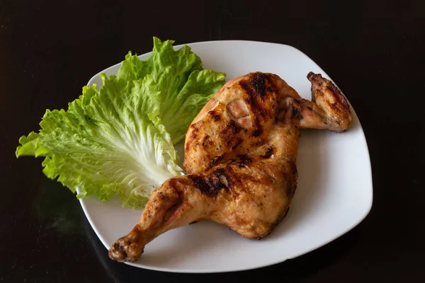 Poulet juteux et frit avec des feuilles de laitue sur une assiette blanche. Fond noir foncé. Gros plan . — Photo