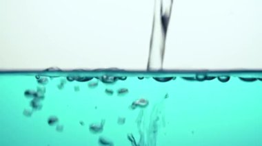 Temiz, şeffaf suyu mavi bir sıvıya döküyor, dalgalanıyor, ampulleri oluşturan cam bir kase içinde. Yakın plan..