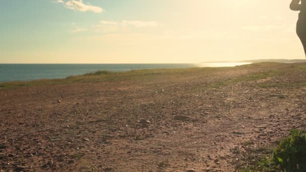 Une femme fait du jogging sur une piste de terre au coucher du soleil près de l'océan. Gros plan . — Video