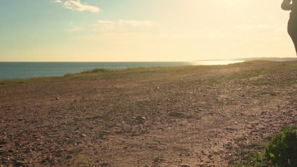 A woman does jogging on a dirt track at sunset day near the ocean. Close-up. — Stock Video