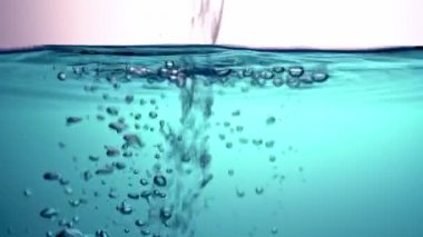 Temiz, şeffaf suyu mavi bir sıvıya döküyor, dalgalanıyor, ampulleri oluşturan cam bir kase içinde. Yakın plan..