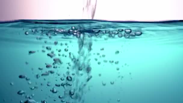 Nalévání čiré, průhledné vody do modré tekutiny, mávat, ve skleněné míse, která vytváří žárovky. Detailní záběr. — Stock video