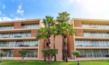Palmiye ağaçları, yeşil çimenler ve mavi gökyüzü olan modern bir otel, güneş. Portekiz, Algarve.