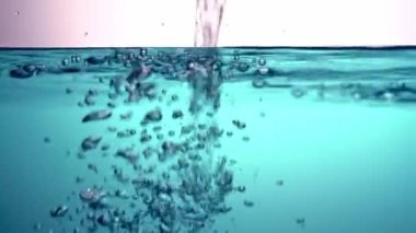 Temiz, şeffaf suyu mavi bir sıvıya döküyor, dalgalanıyor, ampulleri oluşturan cam bir kase içinde. Yakın plan..