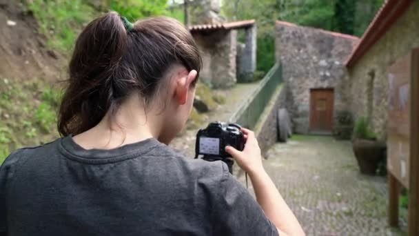 Una joven, fotógrafa, en una zona boscosa, toma fotos de una antigua casa y de una hermosa naturaleza . — Vídeos de Stock