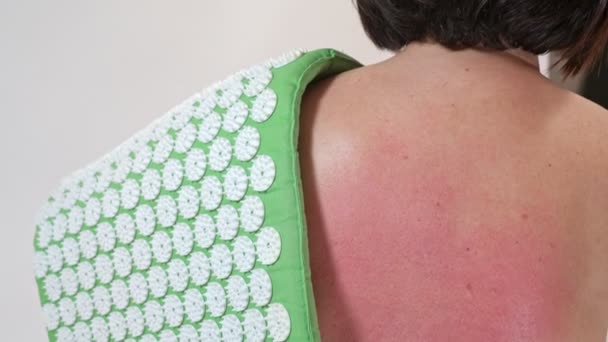 A middle-aged woman punches her red back from a massage for pain in the back and spine on an acupuncture rug. Close-up. — Stock Video