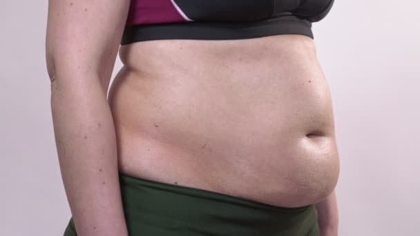 Žena středního věku s povislou pletí se otočí na bok a ukáže své velké břicho na bílém pozadí. Vedlejší plán. — Stock video