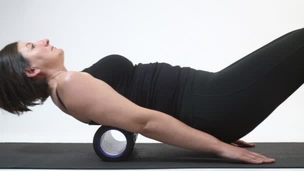 A middle-aged woman is doing a backbone massage on myofascial roller. Close-up. — Stock Video