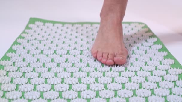 Seorang wanita paruh baya berdiri dengan satu kaki di atas tikar pijat akupuntur. Close-up. — Stok Video