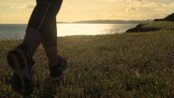 Eine Frau joggt bei Sonnenuntergang auf einem Feldweg in der Nähe des Ozeans. Nahaufnahme. — Stockvideo