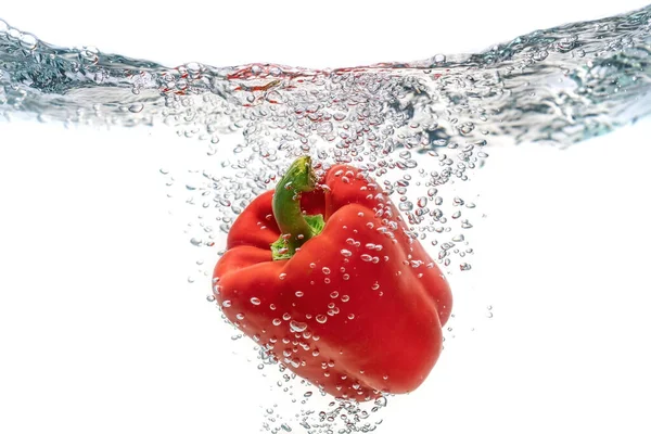 Écologique rouge juteux, le poivre tombant dans l'eau propre crée des bulles. Isolé sur fond blanc . — Photo