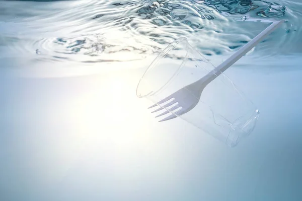The global environmental problem, environmental pollution, waste in the seas and rivers. Plastic cup and fork, under water.
