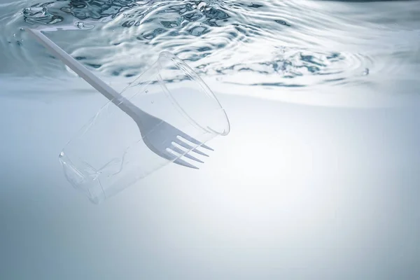 Det globala miljöproblemet, miljöföroreningar, avfall i hav och floder. Kopp och gaffel av plast, under vatten. — Stockfoto