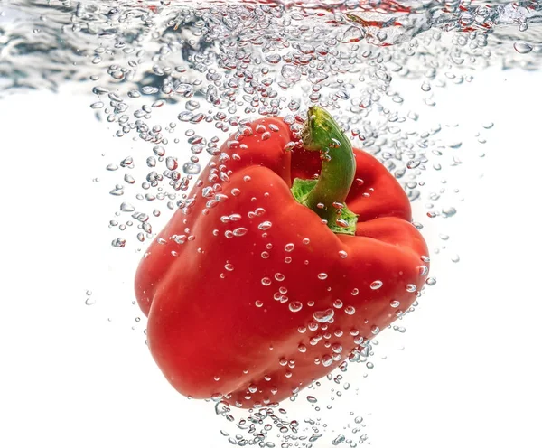 Jugoso rojo ecológico, pimienta cayendo en agua limpia crea burbujas. Aislado sobre un fondo blanco . —  Fotos de Stock