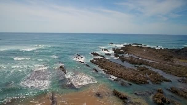 Filmagem de vídeo aéreo. Ondas do oceano batendo em rochas, pedras na praia de Arrifana, Sagres, Portugal, Algarve. Céu azul claro . — Vídeo de Stock