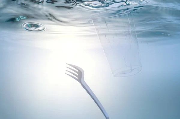 El problema ambiental global, la contaminación ambiental, los residuos en los mares y ríos. Taza y tenedor de plástico, bajo el agua . — Foto de Stock