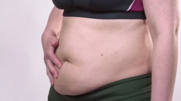 Uma mulher de meia-idade com pele flácida agita uma barriga grande, em um fundo branco. Plano secundário . — Vídeo de Stock