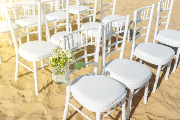 Весільна церемонія на пляжі в сонячний день. Набір білих стільців для гостей, прикрашених квітами . — стокове фото